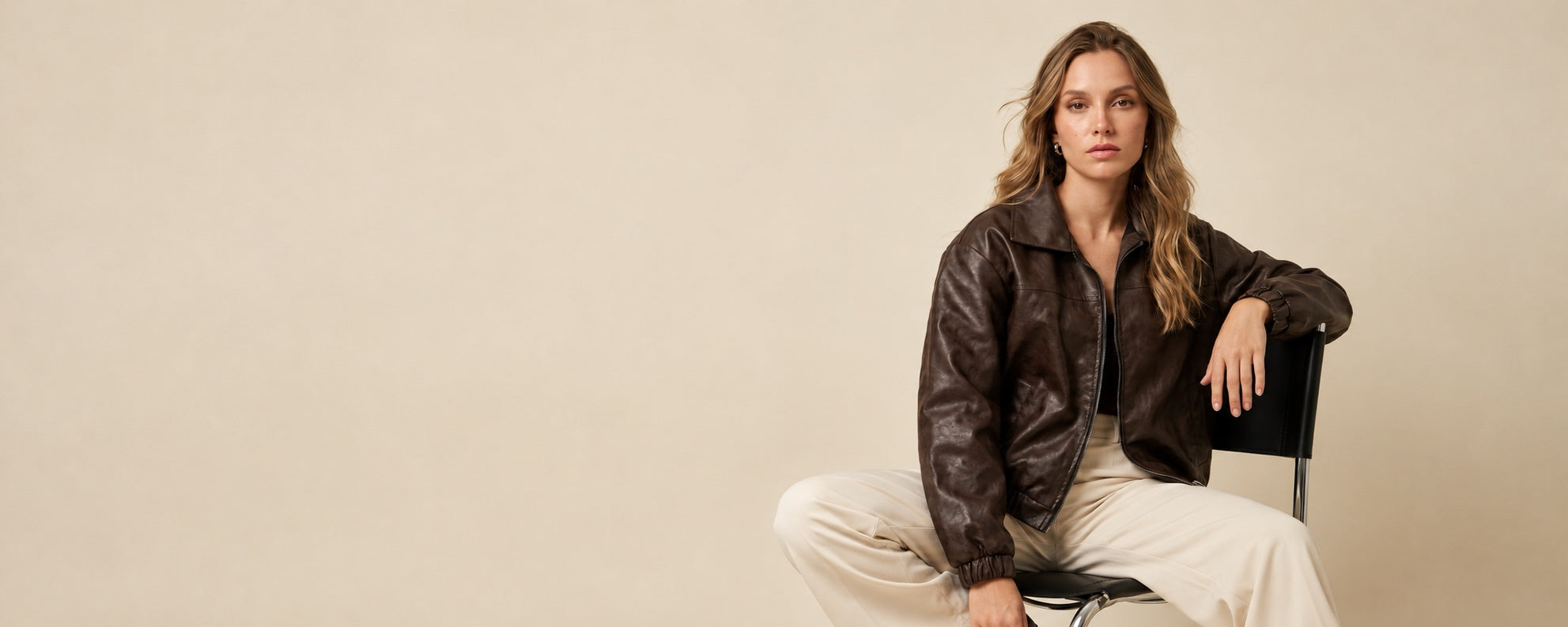 Modelo con chaqueta bomber café de Almmah, sentada sobre un fondo beige.